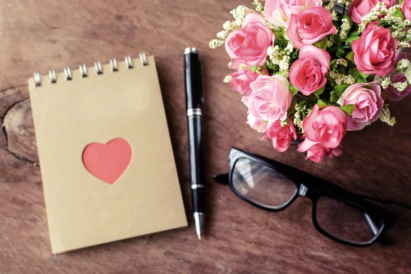 Flower with blank notepad and pen on old wooden background