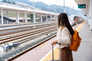 Bagajlı genç bayan turist tren istasyonunda hızlı tren bekliyor.