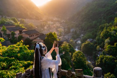 Çinli geleneksel elbiseli genç bayan turist Shangrao, Çin 'deki Wangxian Vadisi' nin güzel gün batımı manzarasının fotoğraflarını çekiyor.