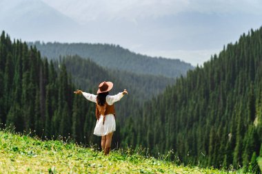 Genç bayan turist, yazın Kalajun 'un Xinjiang otlağındaki renkli çiçeklerle güzel manzaranın tadını çıkarıyor ve dinleniyor.