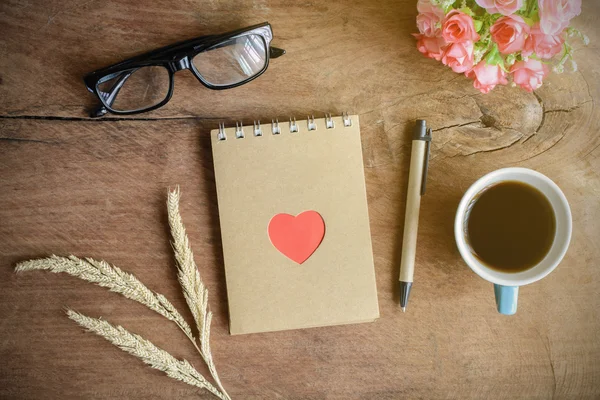 Cup of coffee with flower and blank notebook on wooden table