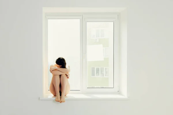 Sad woman hug her knee and cry on window