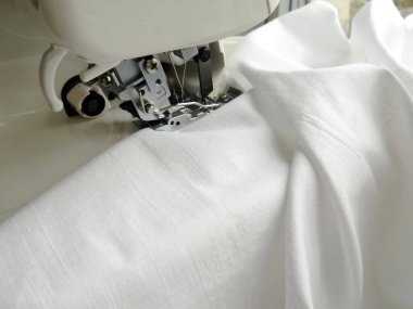 Dikiş makinesi beyaz kumaş dikiyor. Kumaş kenarlarını kilitleyin. Kumaş endüstrisi