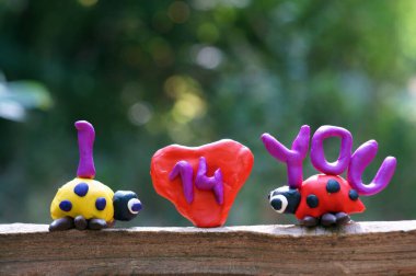 Plastikten yapılmış iki uğur böceği figürü. Aralarında bir kalp var. Yanındaki yazıda seni seviyorum yazıyor..