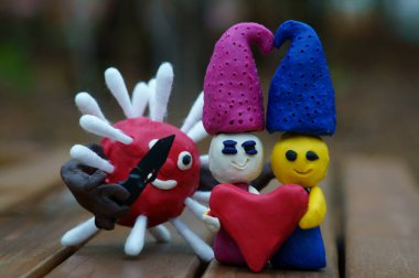 Kil içinden bir kalp tutan iki cüce. Yanında bıçaklı bir virüs figürü var..