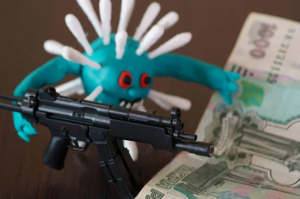 Virus figurine made of plasticine with toy weapons. Next to it are paper banknotes.