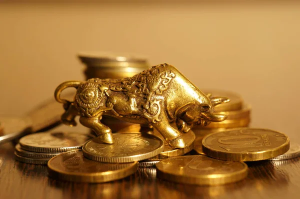 Metal bull with coins on a gold background. Financial symbol.