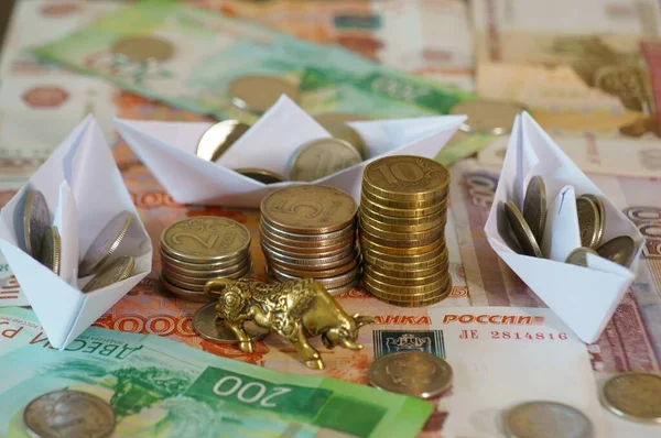 Metal bull with coins on the table. Near paper boats with coins.