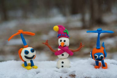 Plastikten yapılmış kırmızı şapkalı bir kardan adam figürü. Oyuncak helikopterlerin yanında..