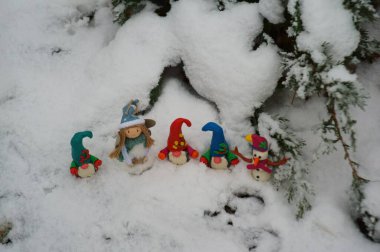 Karlı bir ormanda renkli cücelerin figürleri. Bir kardan adam ve oyuncak bir meleğin yanında..