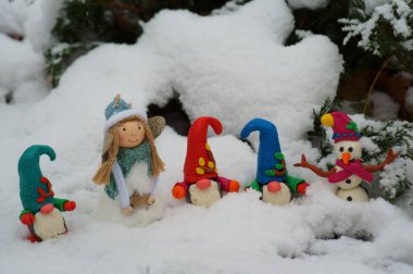 Karlı bir ormanda renkli cücelerin figürleri. Bir kardan adam ve oyuncak bir meleğin yanında..