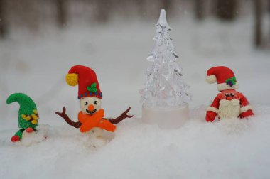 Noel Baba figürü, kardan adam ve kardan cüce. Yanında oyuncak bir Noel ağacı var..