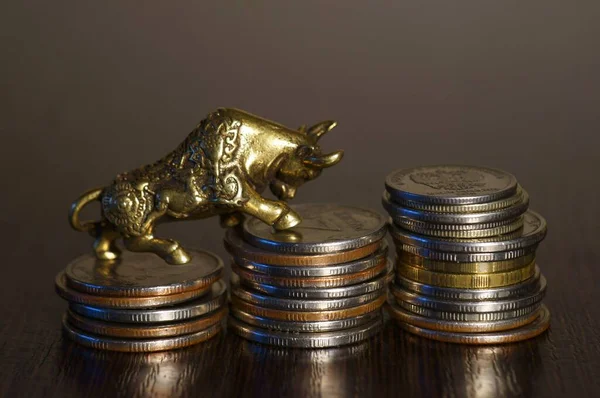 Metal bull figurine close-up. Next to it is a stack of coins. A financial symbol.