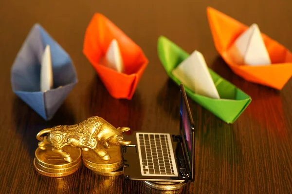 A metal bull with a laptop and a group of colorful paper boats on the table. Business concept.