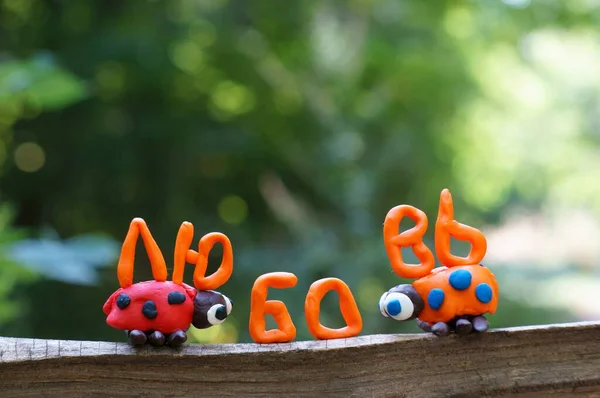 The inscription love in the Russian language. Next to it are two figures of ladybirds made of plasticine.