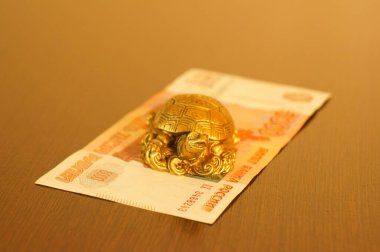 Metal kaplumbağa bilgeliğin sembolüdür. Yanında bir banknot var..