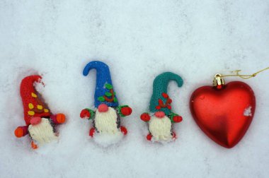 Beyaz karlı arka planda üç cüce figürü. Yanında oyuncak bir kalp var..