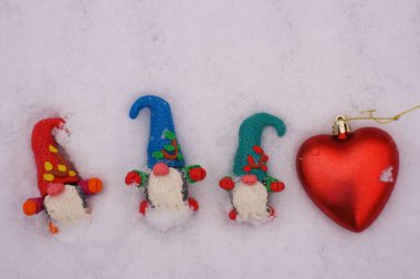 Beyaz karlı arka planda üç cüce figürü. Yanında oyuncak bir kalp var..