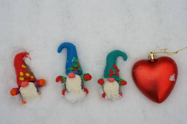 Beyaz karlı arka planda üç cüce figürü. Yanında oyuncak bir kalp var..