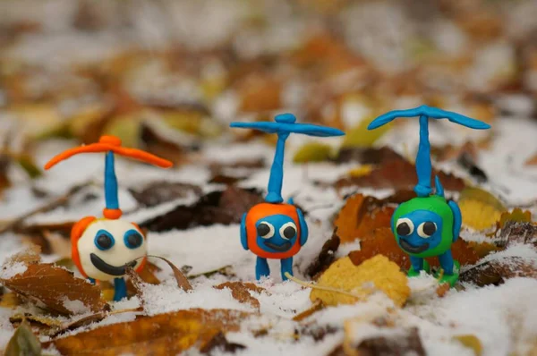 Karda sonbahar yapraklarının arka planında üç oyuncak renkli helikopter..