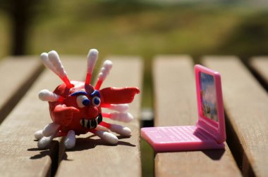 Plastikten yapılmış bir koronavirüsün yakın plan figürü. Yanında oyuncak bir laptop var. İş konsepti.