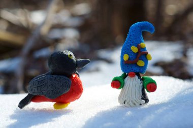 Bir cüce heykeli ve karlı bir ormanda plastik bir serçe..