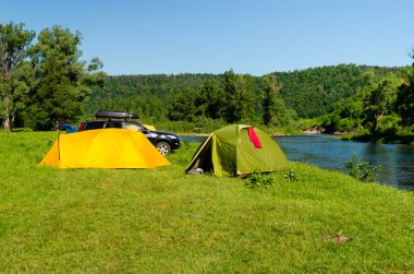 Tourist camp with tents and car on the river bank clipart