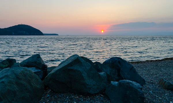 Puesta de sol sobre el mar y las rocas en la orilla — Foto de Stock