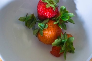 Beyaz tabakta yaprakları olan çilekler.