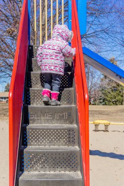 Bir çocuk halk parkında binicilik ekipmanının merdivenlerinden çıkıyor.