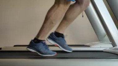 Spor merkezinde spor ayakkabılı bir adamın spor bisikleti üzerinde koşması..