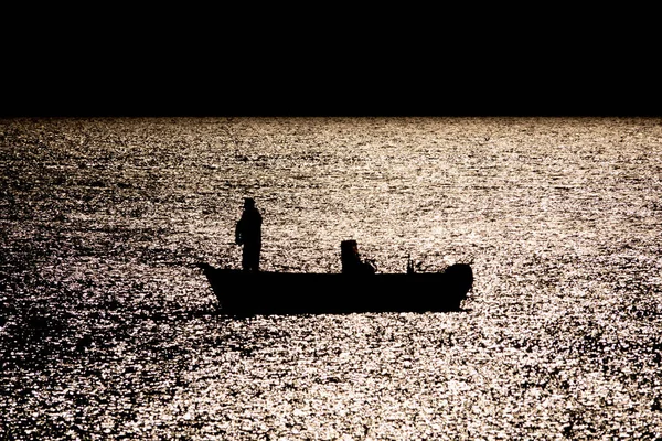 Silhouette of boat fishing in the sea in moonlight reflection reverse light