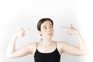 Genç ve güzel bir kadın beyaz arka planı düşünürken parmaklarıyla işaret ediyor.