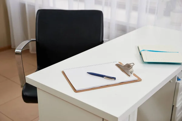 Стул и пустой буфер обмена и ручка на столе в офисе — стоковое фото