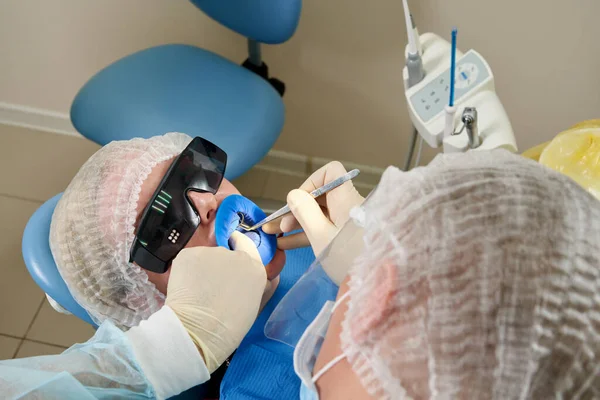 Tandarts doet een tandheelkundige behandeling bij een vrouwelijke patiënt. Tandarts onderzoekt een patiënt tanden in de moderne tandheelkunde kantoor — Stockfoto