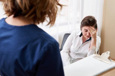 Doktor genç bayan hastayla konuşuyor ve yanında durup notlar alıyor.