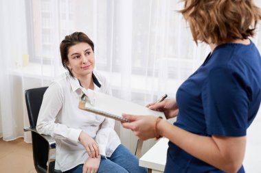 Doktor genç bayan hastayla konuşuyor ve yanında durup notlar alıyor.