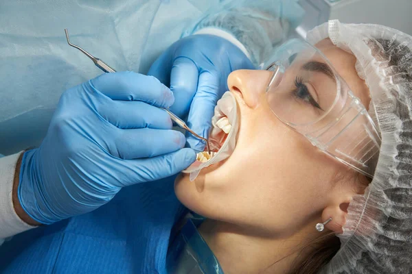 Tandläkare som gör en tandvård på en kvinnlig patient. Tandläkare undersöker en patient tänder i modern tandvård kontor — Stockfoto