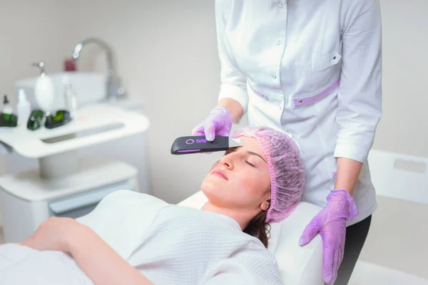 Hands of cosmetologist making ultrasound facial cleaning with special machine — Stock Photo, Image