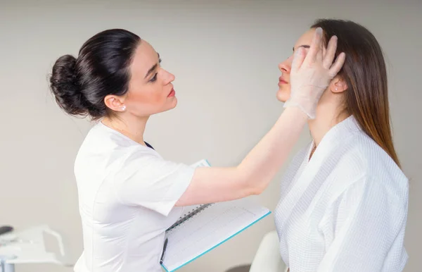 Professional cosmetician examining face skin of girl in clinic of esthetic cosmetology — Stock Photo, Image