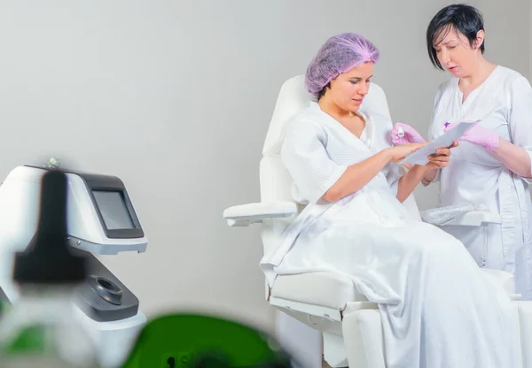 Kobieta w salonie piękności omówić leczenie anti-aging z kosmetologiem patrząc przez magazyn — Zdjęcie stockowe