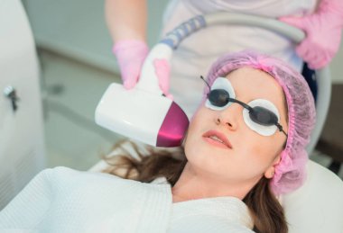 Genç bir kadın kozmetoloji kliniğinde lazer tedavisi görüyor. Koruyucu gözlüklerle kaplı gözler.