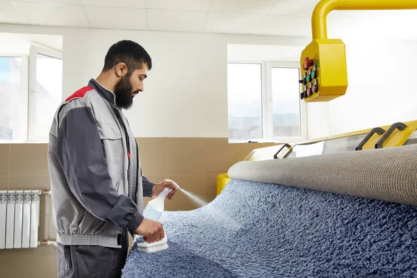 Hombre con uniforme de pulverización de detergente en la alfombra azul para quitar manchas en el servicio de limpieza profesional —  Fotos de Stock