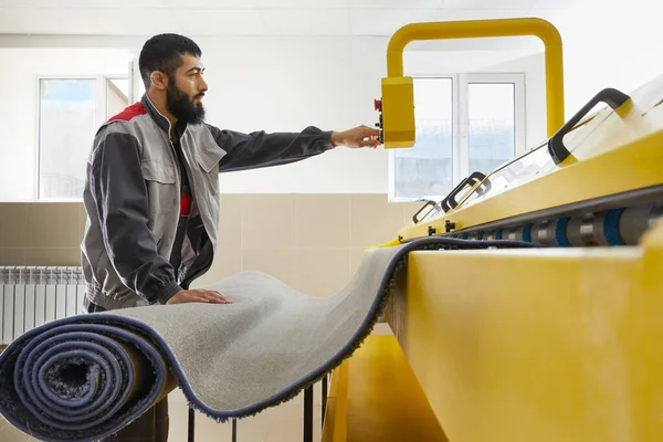 Man operating carpet automatic washing machine in professional laundry service