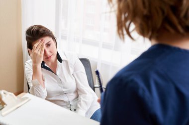 Doktor genç bayan hastayla konuşuyor ve yanında durup notlar alıyor.