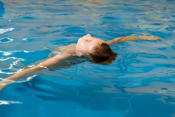 Niño nadando en piscina cubierta divirtiéndose durante la clase de natación — Foto de Stock