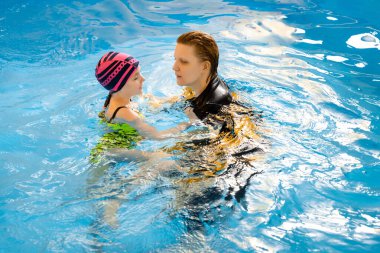 Koç, çocuklara yüzme havuzunda yüzmeyi ve dalmayı öğretiyor.