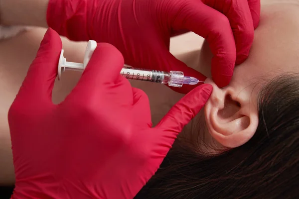 Cosmetologist doctor makes the injections procedure in ear for smoothing wrinkles and against flabbiness of the skin on earlobe of a beautiful, young woman — Stock Photo, Image