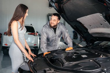 Araba tamircisi ve müşteri servis edilen arabanın yanında dururlar.