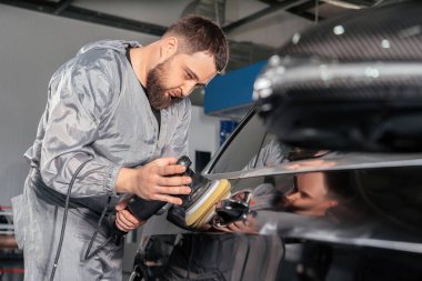 Araba tamircisi özel öğütücüyle araba cilalıyor ve araba tamirhanesindeki çiziklerden dolayı cila yapıyor. Profesyonel araba temizleme ve bakım konsepti